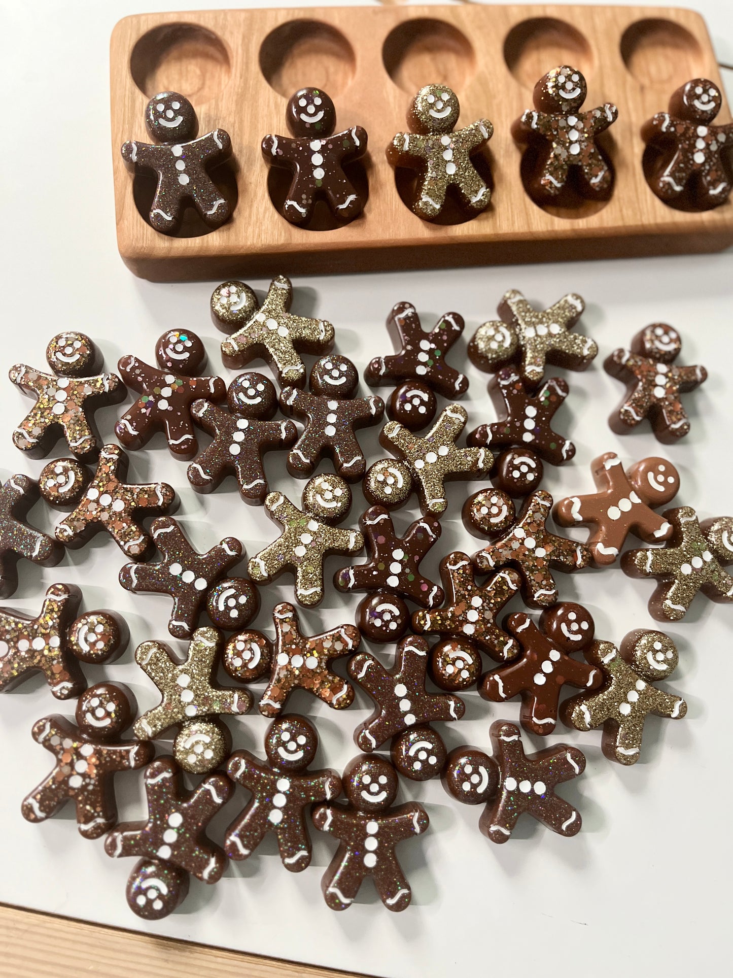 Chocolate resin gingerbread men on a white surface with a wooden ten frame in the background.