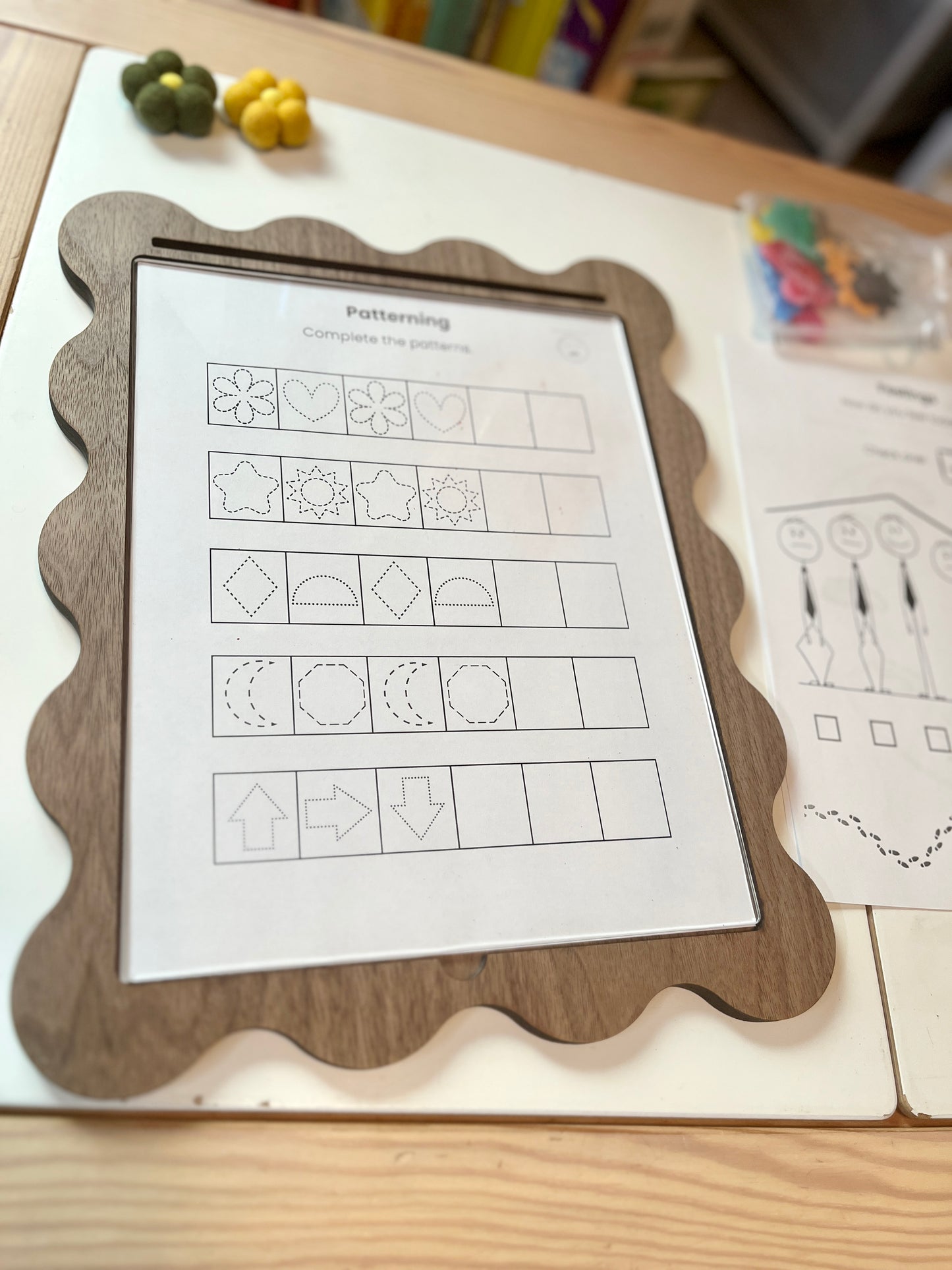 Educational worksheet on a wooden frame with pattern recognition activity, surrounded by educational materials.
