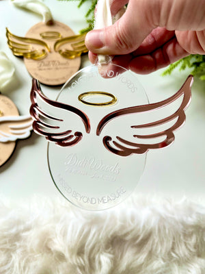 Hand holding clear acrylic angel wing ornament with gold halo and engraved memorial text on white background