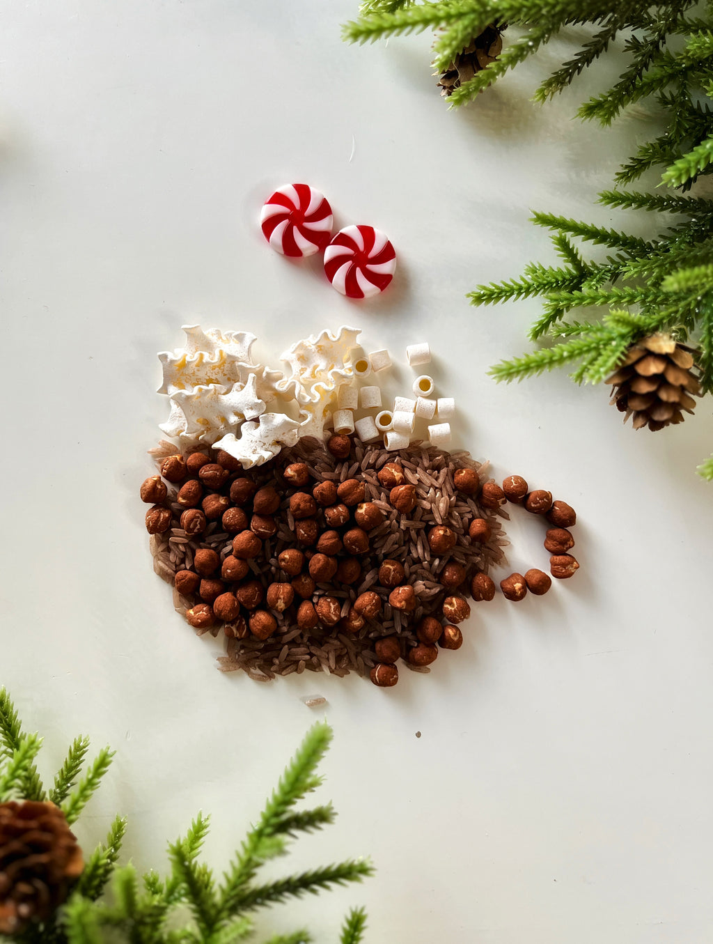 Hazelnuts and rice forming a cup shape with white beads, popcorn, red and white peppermint candies, and pine greenery nearby