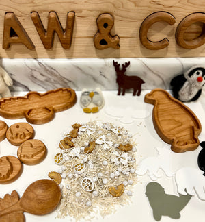 Carved wooden animal-shaped trays with natural pasta pieces and small white decorative balls on white marble surface