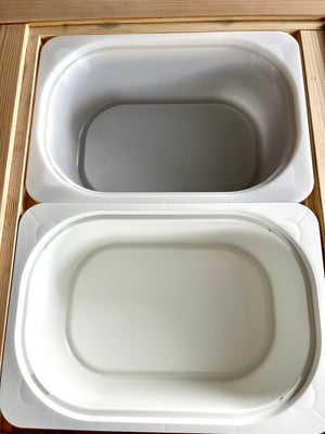 Small and large white plastic Trofast bins nested inside wooden Flisat table frames on wooden surface