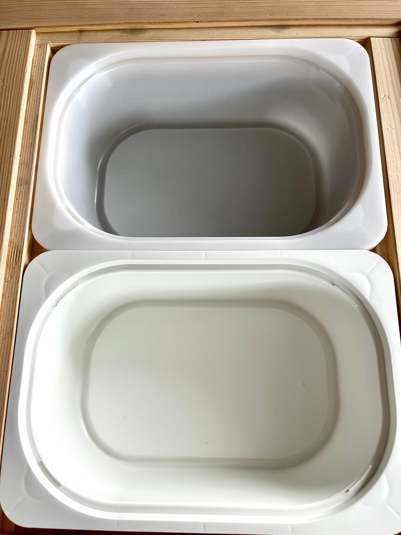 Small and large white plastic Trofast bins nested inside wooden Flisat table frames on wooden surface