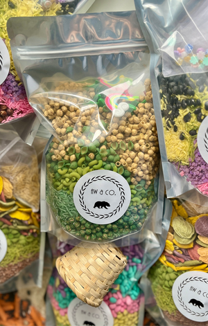 Clear resealable bag with green pasta, wooden beads, and small rainbow and cloud shapes inside and around it