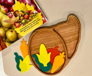 Wooden divided plate shaped like a cornucopia with colorful wooden vegetable pieces and a fruit-themed book on beige surface