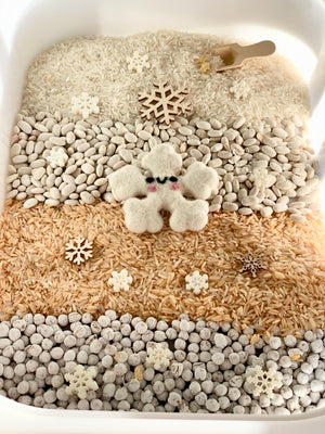Winter sensory kit with layered rice, beans, snowflake shapes, and a felt snowflake character in a white bin
