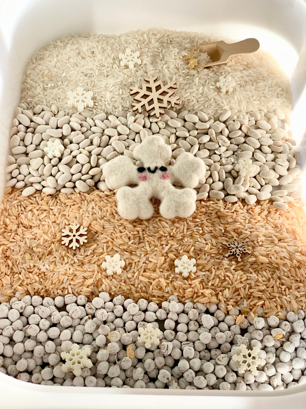 Winter sensory kit with layered rice, beans, snowflake shapes, and a felt snowflake character in a white bin