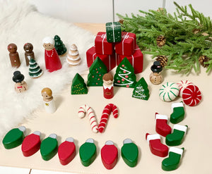 Set of wooden Christmas trees with holiday peg dolls, candy canes, stockings, presents, and pine branch on white surface