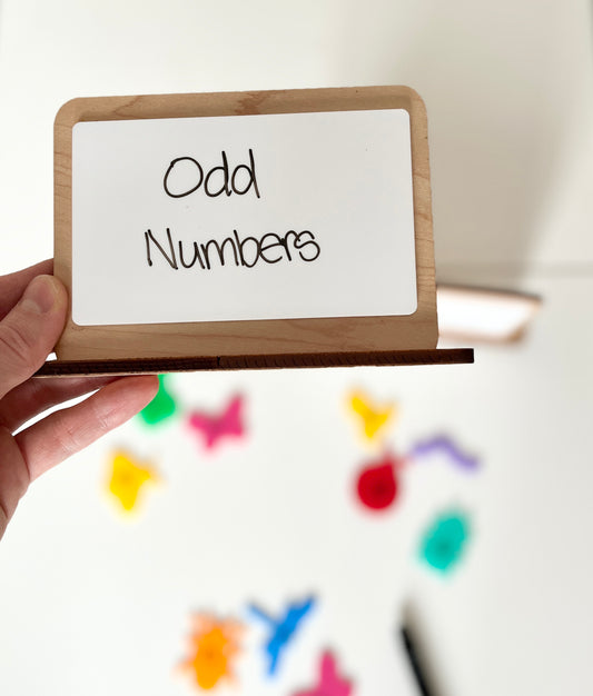 Hand holding a small whiteboard with 'Odd Numbers' text against a colorful background