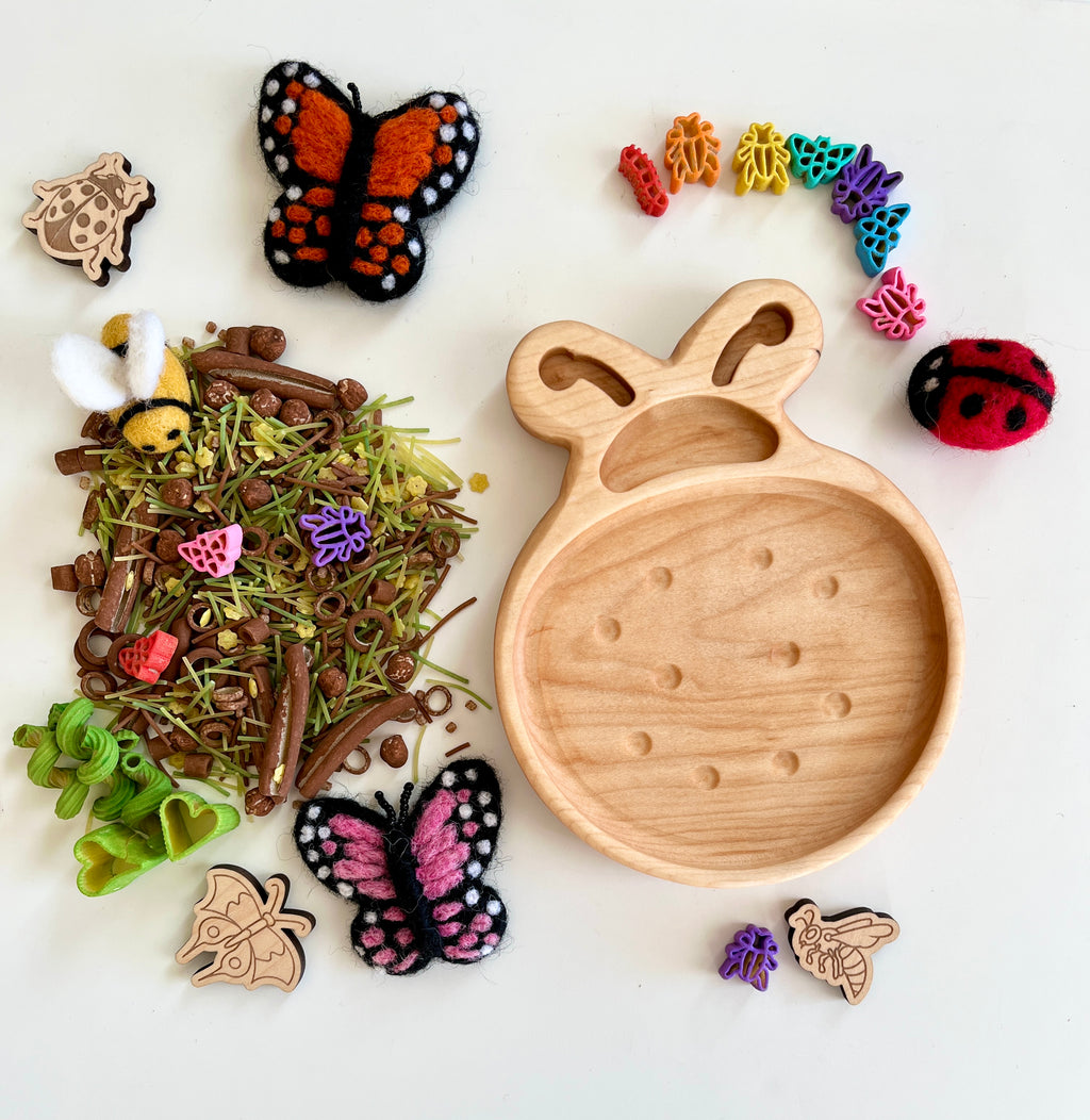Wooden bee-shaped tray with colorful insect-themed beads, felt butterflies, wooden insect cutouts, and natural craft materials on white background
