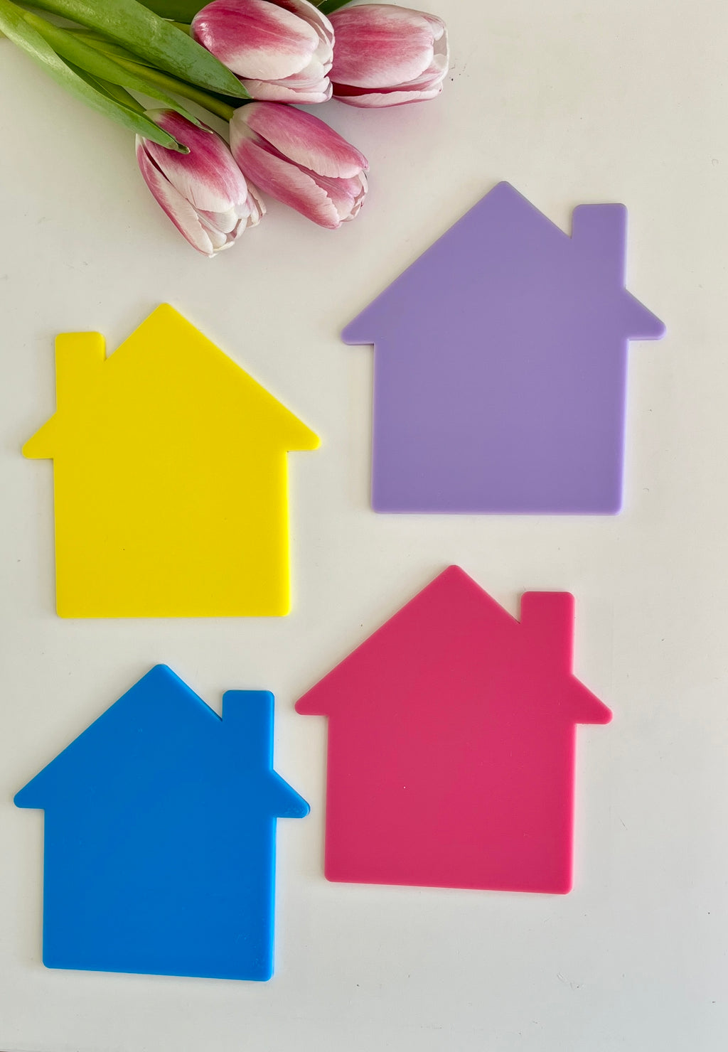 Four colorful house-shaped cutouts in yellow, purple, blue, and pink with pink tulips on white background