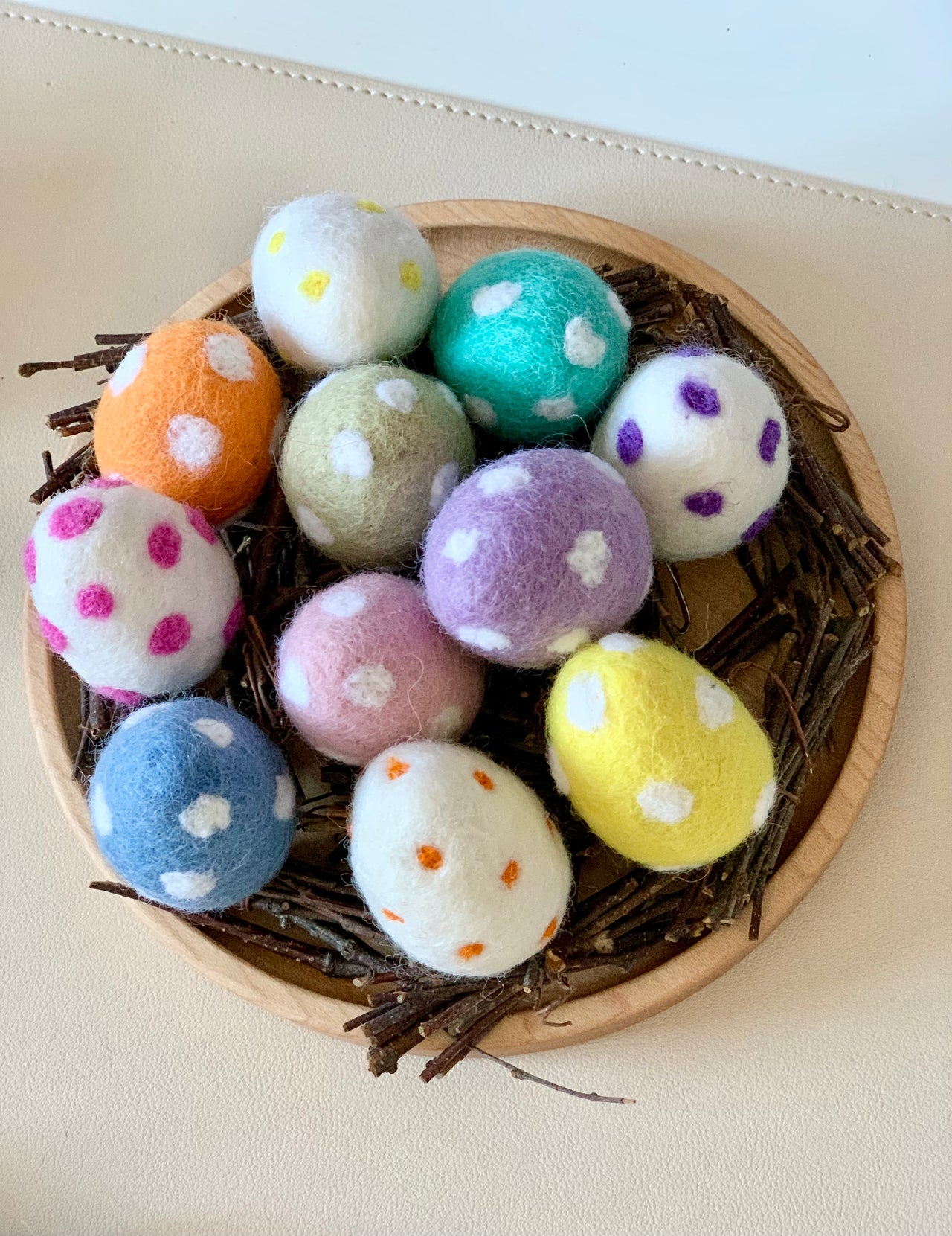 Round wooden tray filled with felt eggs in various colors and spotted patterns resting on twigs
