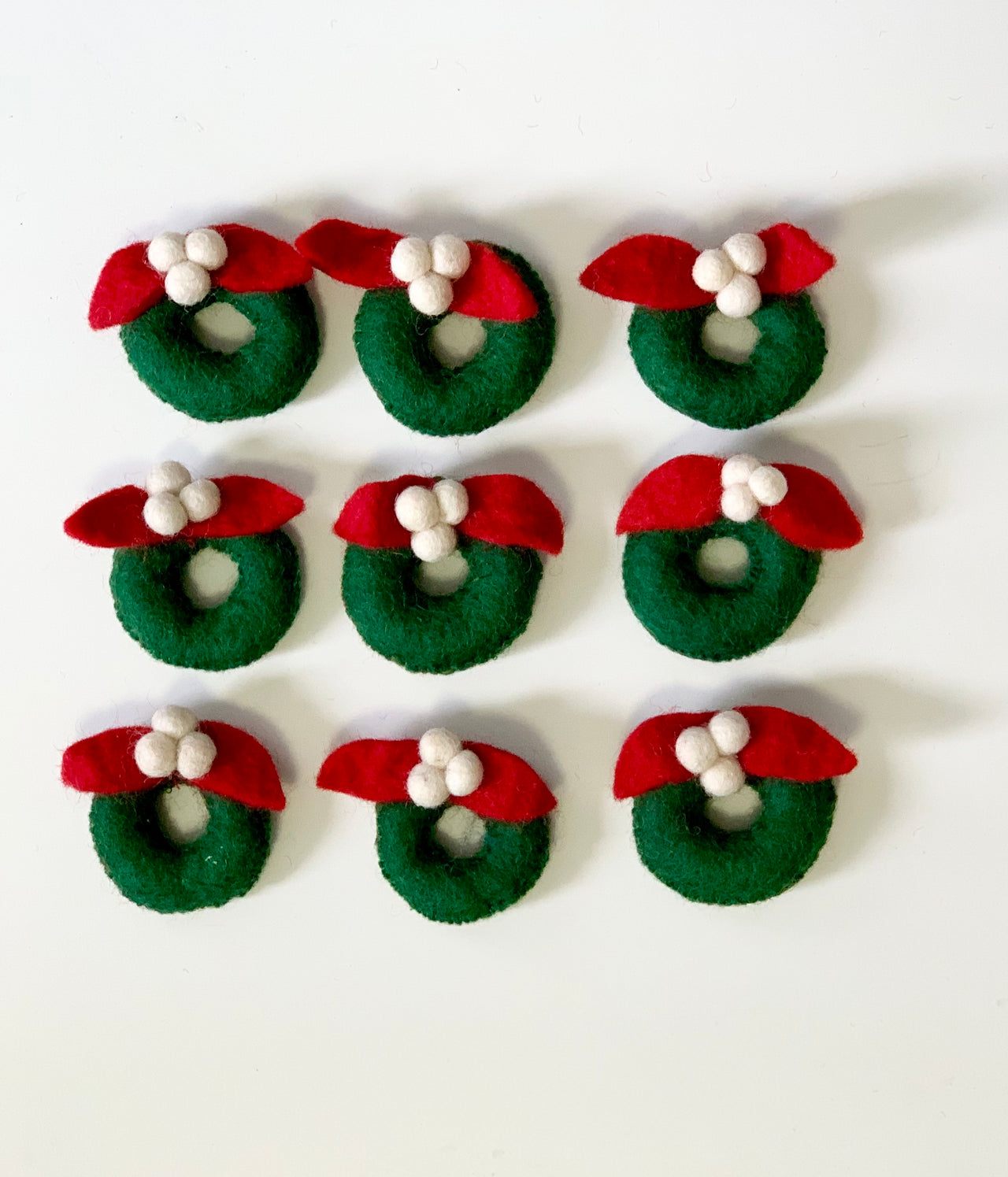 Set of handmade green felt wreaths with red leaves and white berries on white background arranged in rows