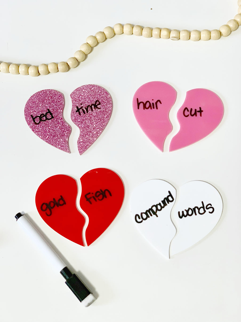 Four pairs of colorful broken heart-shaped boards with matching words and a black dry erase marker on white surface