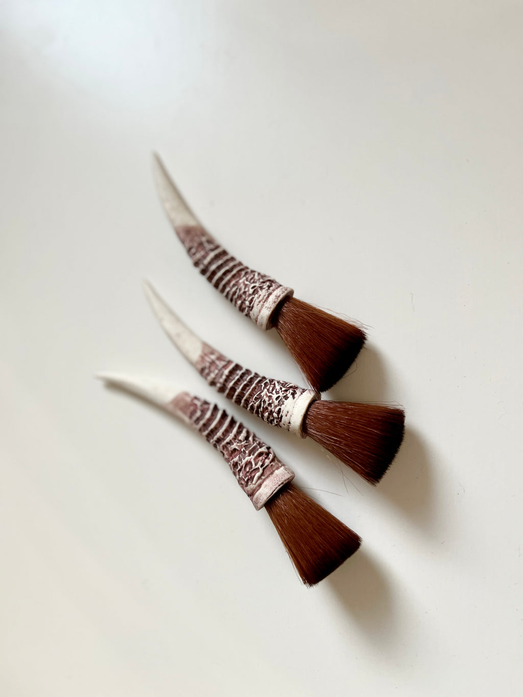 Three small angled brushes with textured ivory handles and dense brown bristles on a plain white background