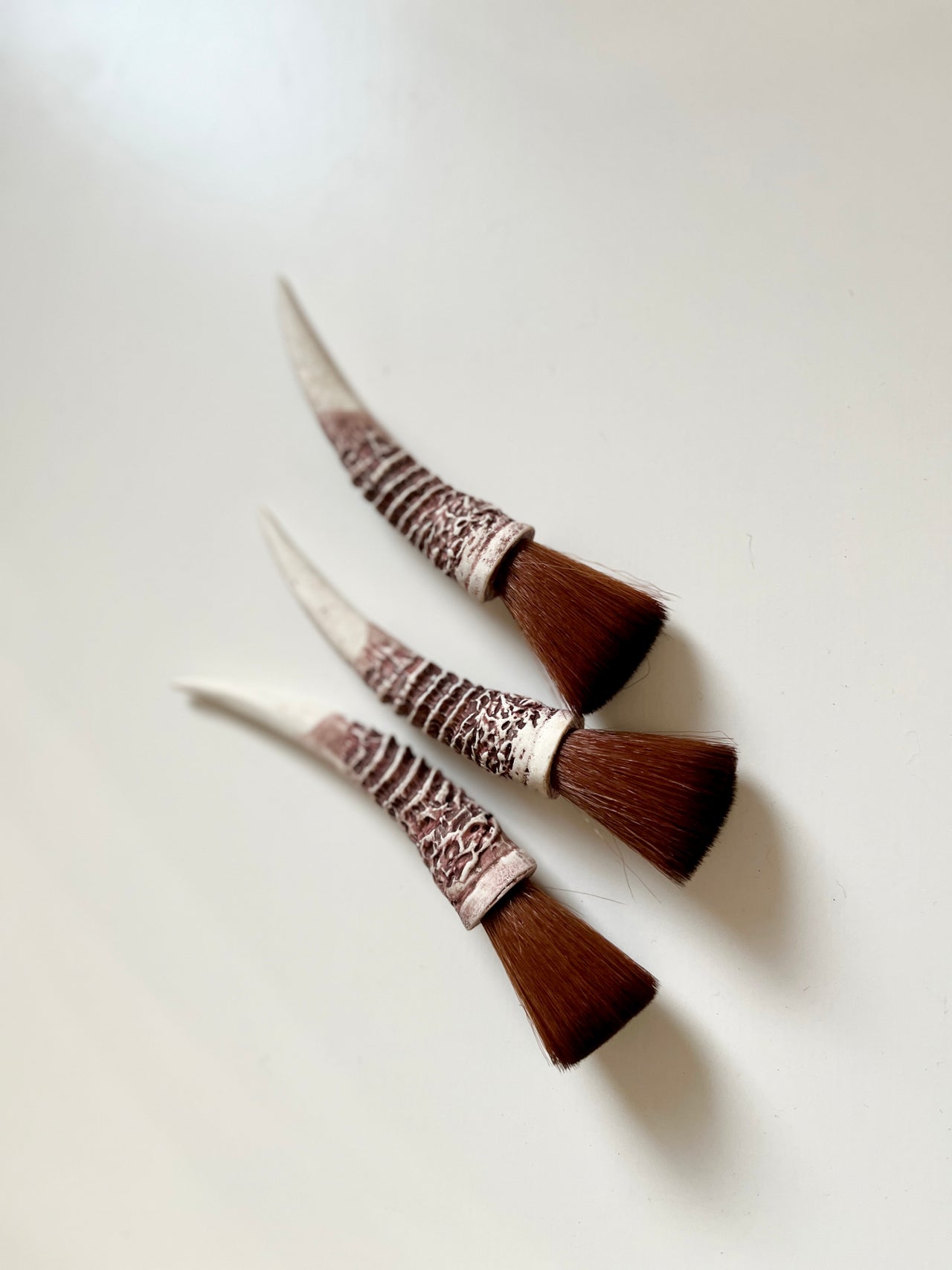 Three small angled brushes with textured ivory handles and dense brown bristles on a plain white background
