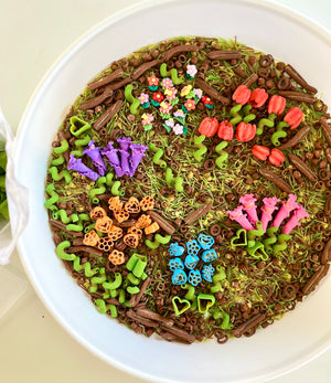 Round white bowl filled with colorful floral-shaped pasta and green spirals on dried grass and brown pasta mix