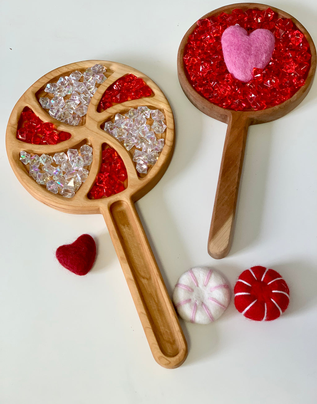 Wooden sensory trays filled with red and clear acrylic gems and pink and red felt heart shapes on white surface