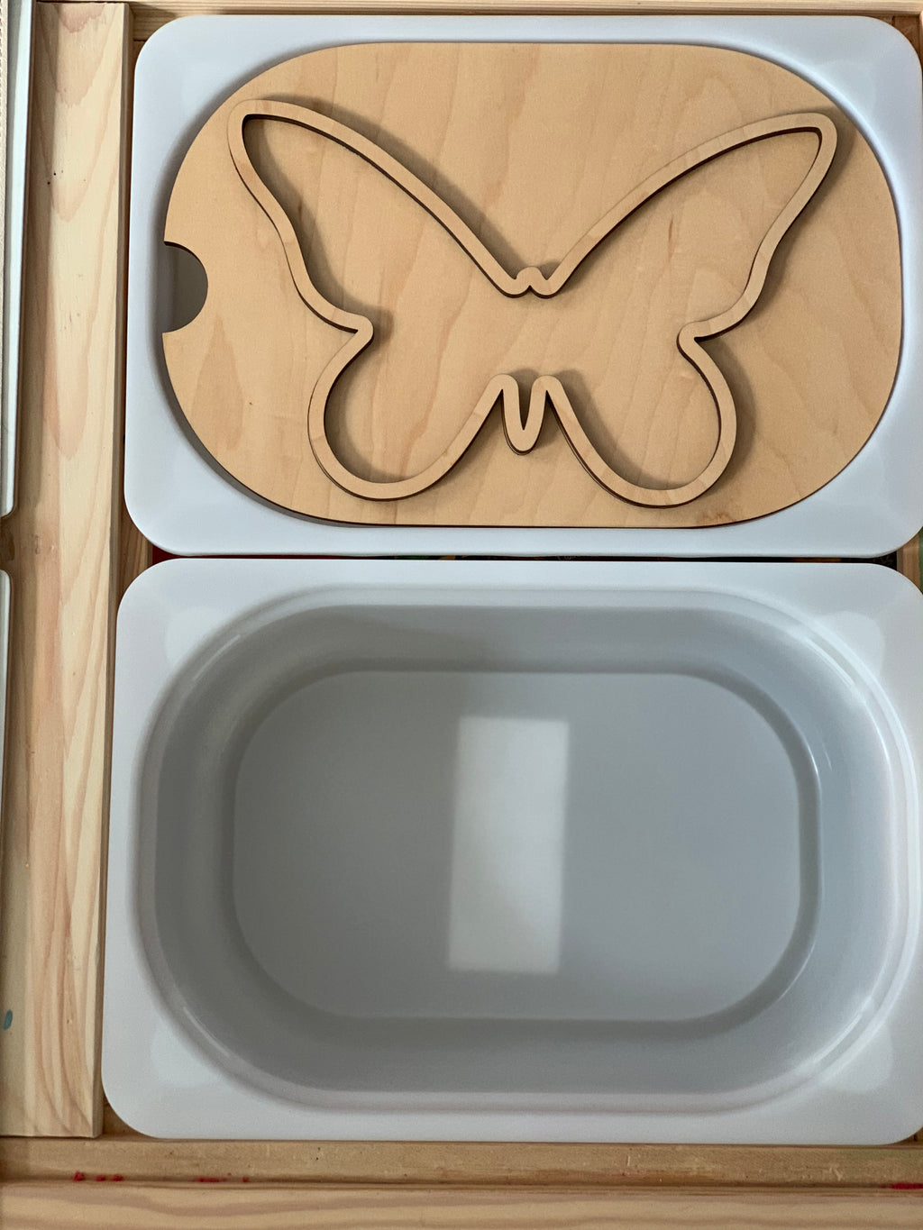 Small butterfly-shaped wooden Flisat table top insert with white plastic bin in wooden frame on light surface
