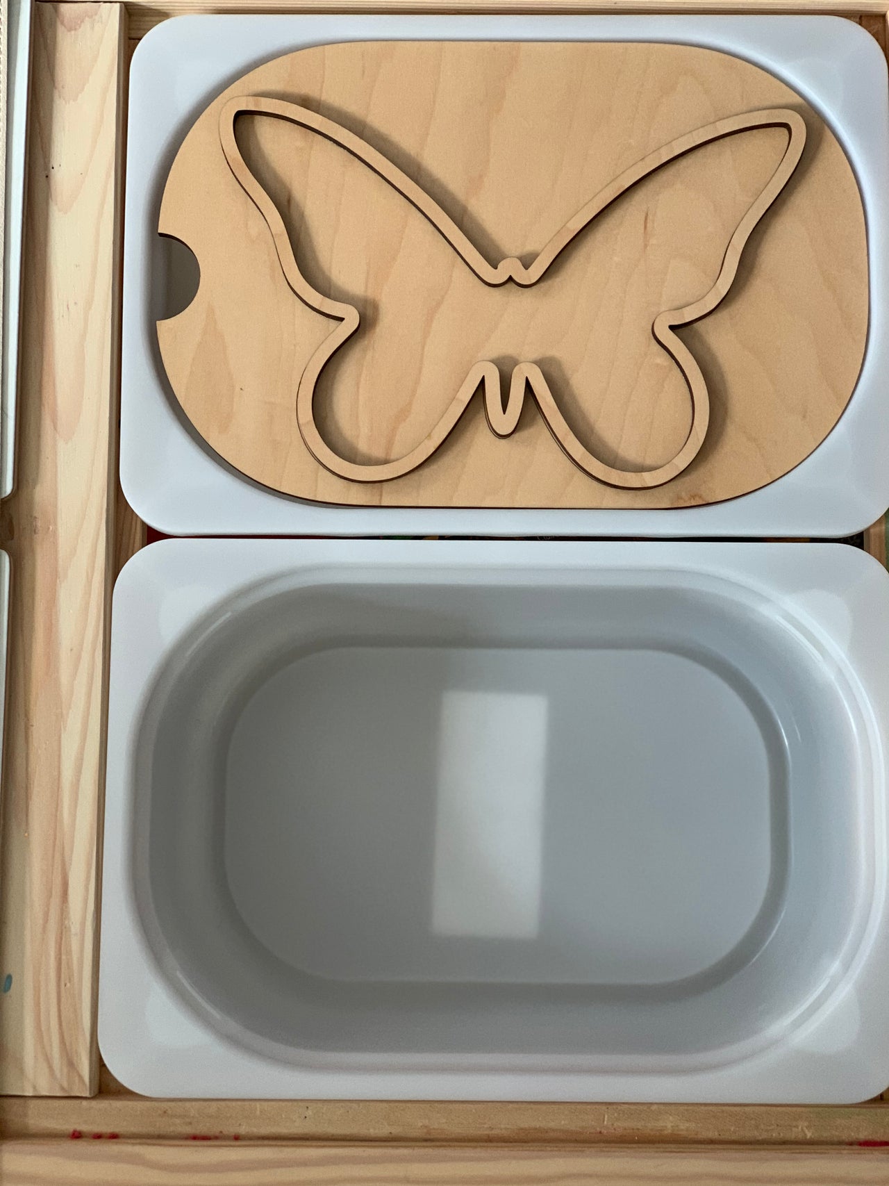Small butterfly-shaped wooden Flisat table top insert with white plastic bin in wooden frame on light surface