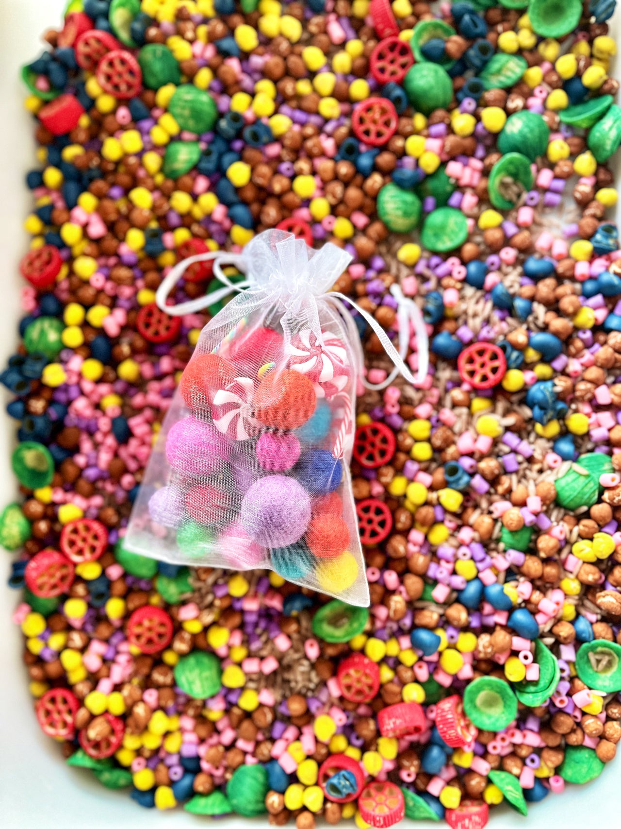 Small organza bag filled with colorful felt balls and candy-shaped beads on a vibrant mix of beads background