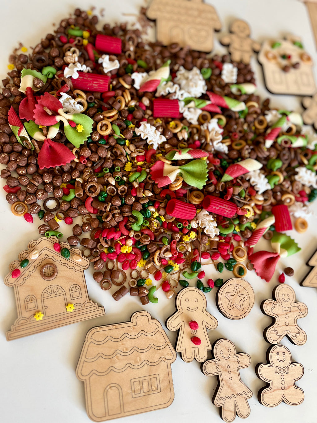 Assortment of wooden gingerbread cutouts surrounded by colorful pasta and small decorative holiday beads on white surface