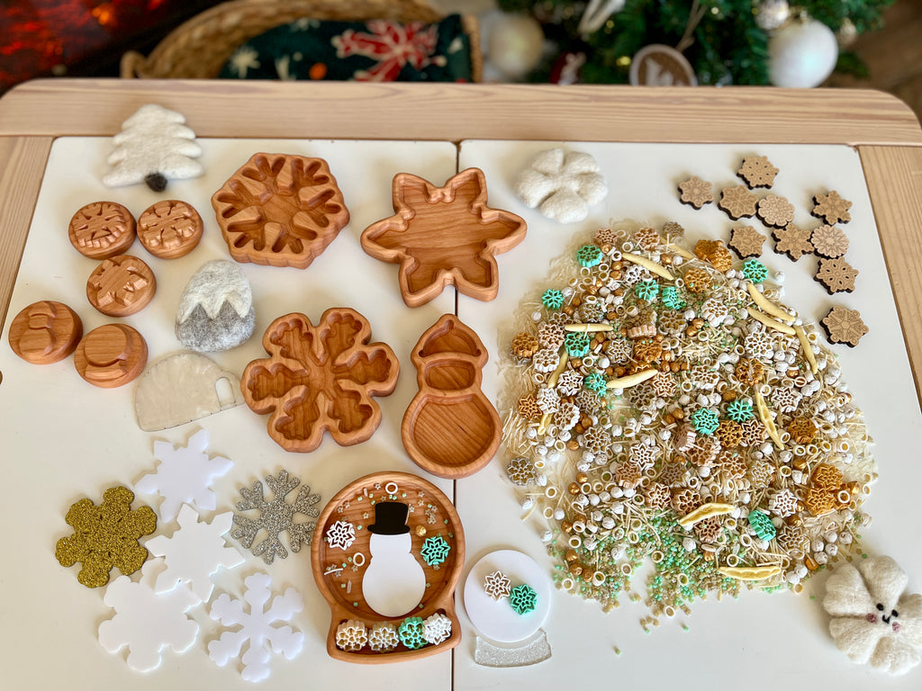 Collection of wooden trays shaped like winter items and assorted small winter-themed decorations on a white surface