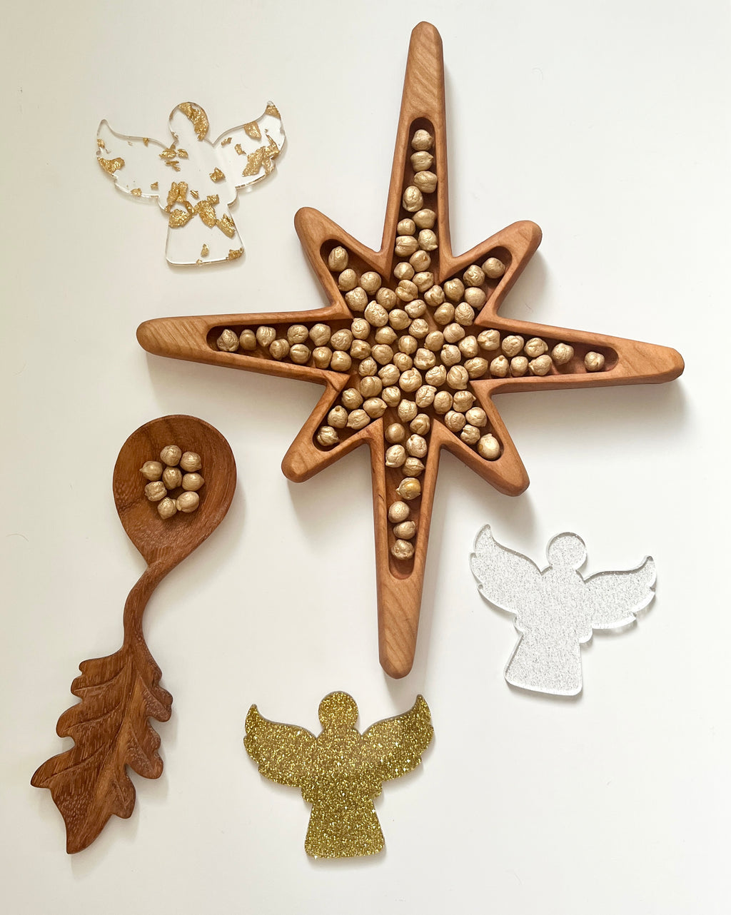 Star-shaped wooden tray filled with hazelnuts next to wooden spoon and three decorative angel cutouts