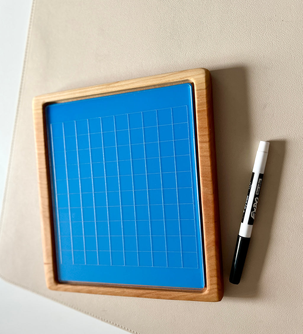 Blue grid drawing board with natural wooden frame and black and white dry erase marker on beige surface