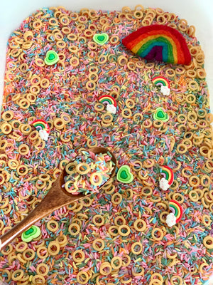 Colorful rice and small ring pieces mixed with green heart and rainbow shapes in white container with wooden spoon and rainbow toy