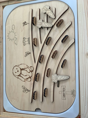 Wooden game board with carved bunny, carrot pieces, flower designs, and labeled carrot patch area on light wood surface