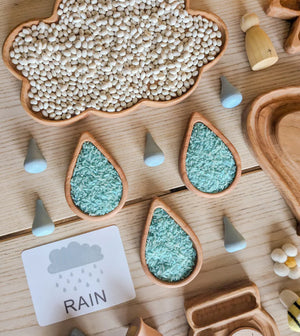 Wooden rain drop plates filled with blue rice and wooden cloud tray filled with white beans on light wood surface