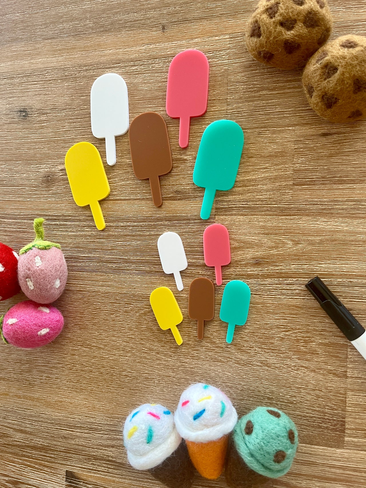 Little Dry Erasables - Popsicles featuring handcrafted wooden popsicle shapes in assorted bright colors arranged on a wood surface with felt food pieces and a black marker, homeschool education resources.