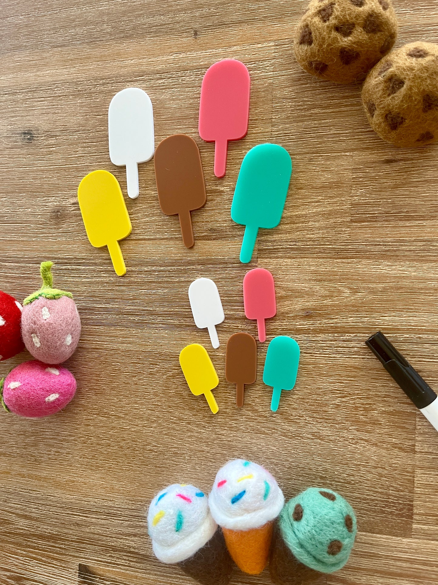 Little Dry Erasables - Popsicles featuring handcrafted wooden popsicle shapes in assorted bright colors arranged on a wood surface with felt food pieces and a black marker, homeschool education resources.