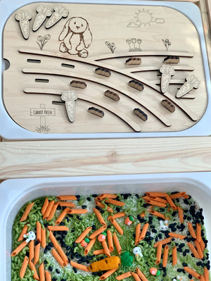 Wooden carrot patch game board with bunny illustration and movable carrot and bunny-shaped pieces above a sensory bin with pasta and beans