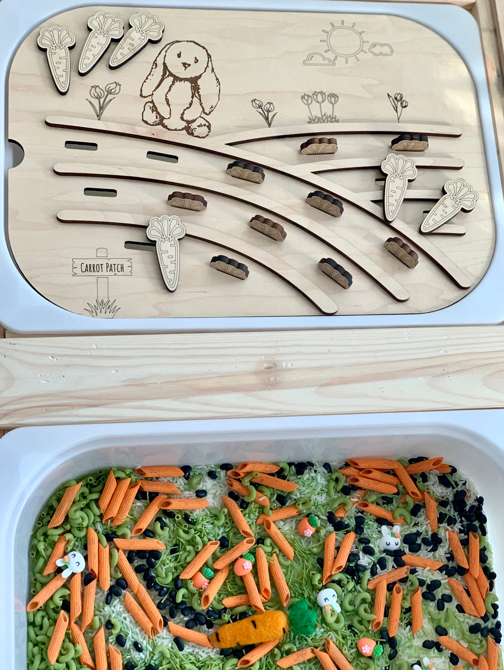 Wooden carrot patch game board with bunny illustration and movable carrot and bunny-shaped pieces above a sensory bin with pasta and beans