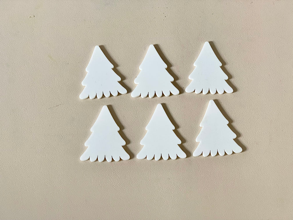 Set of six white pine tree-shaped dry erasable wooden pieces on beige surface with smooth finish