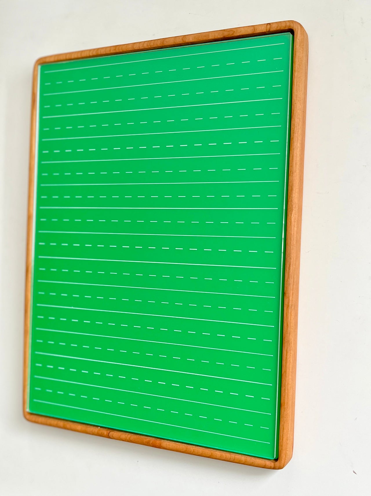Tall rectangular wooden sensory tray holding green dry erase insert with white dashed handwriting lines on white background