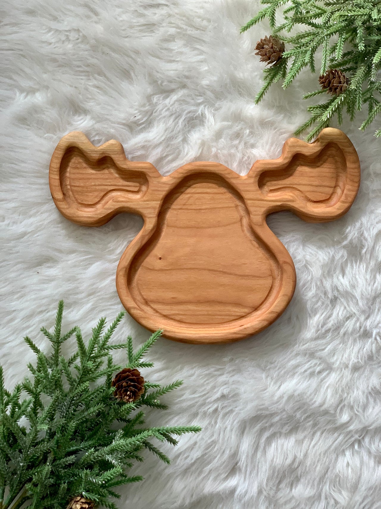 Wooden moose-shaped sensory tray on soft white fur with pine branches and pinecones around edges
