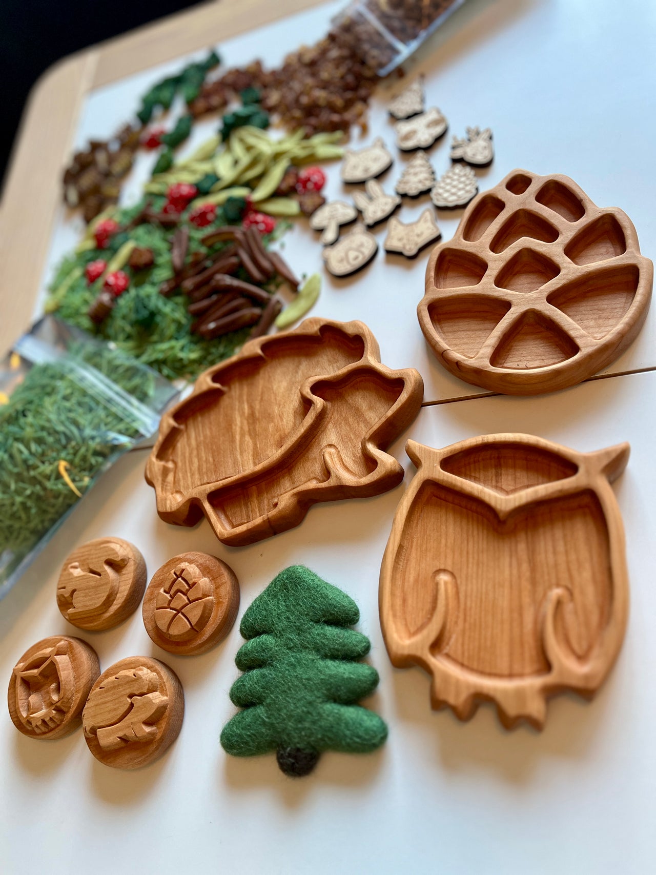 Set of six wooden mini woodland trays shaped like hedgehog, owl, pinecone, tree, and nature tokens on white surface