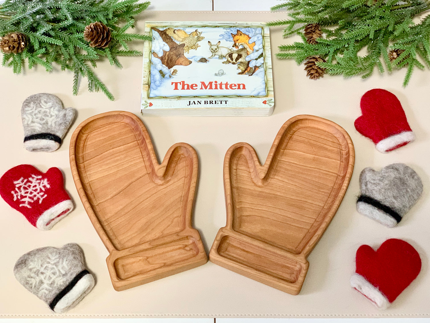 Pair of wooden mitten-shaped sensory trays surrounded by small colorful felt mittens and a children's book on white surface
