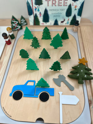 Wooden playset with blue truck, green tree shapes, gray axe, white flag, and felt Christmas tree with yellow star on wood board