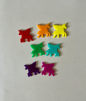 Seven small colorful unicorn-shaped plastic pieces in red, orange, yellow, green, blue, purple, and pink on a light surface