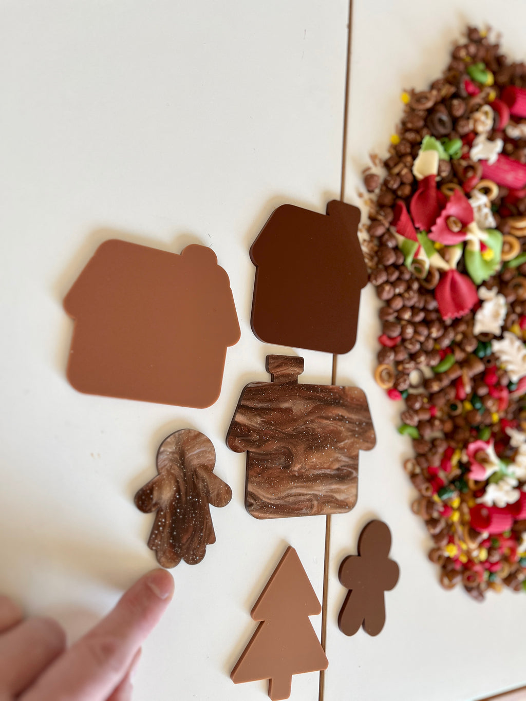 Brown and marbled house and holiday-themed cutouts with colorful sensory materials nearby on white surface