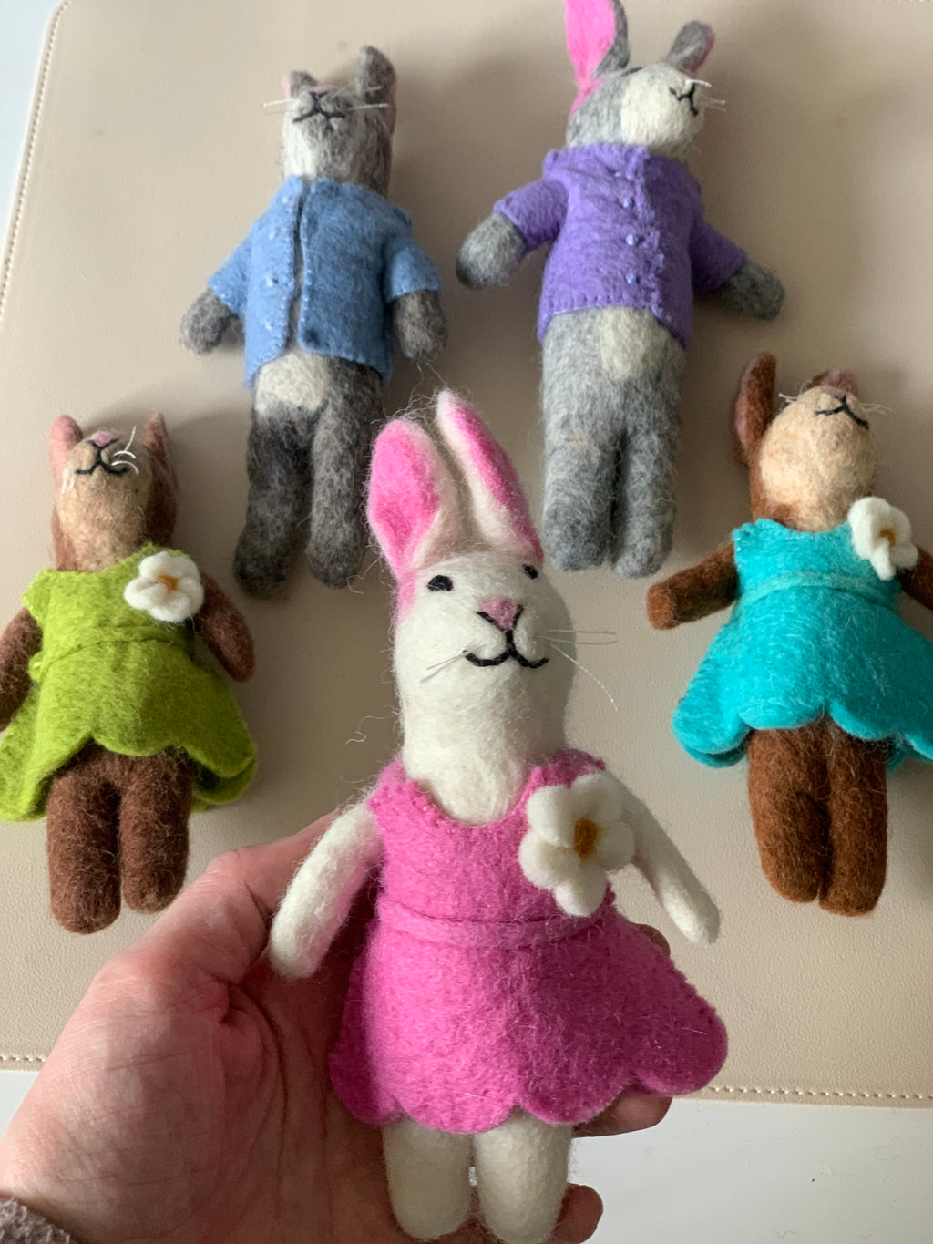 Handfelt bunny dolls with pink, green, and blue dresses and gray bunnies in blue and purple tops on a beige surface