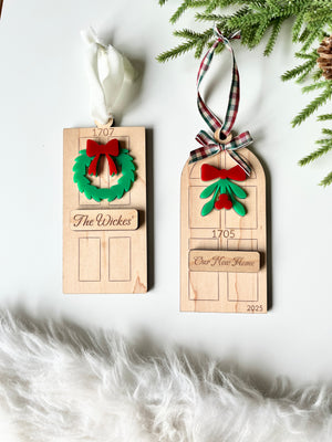 Two wooden door-shaped ornaments featuring green wreaths, red bows, personalized plaques, and fabric ribbons on white background