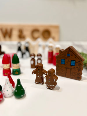 Gingerbread man and woman figurines with wooden house, elf dolls, and colorful cone-shaped decorations on white surface