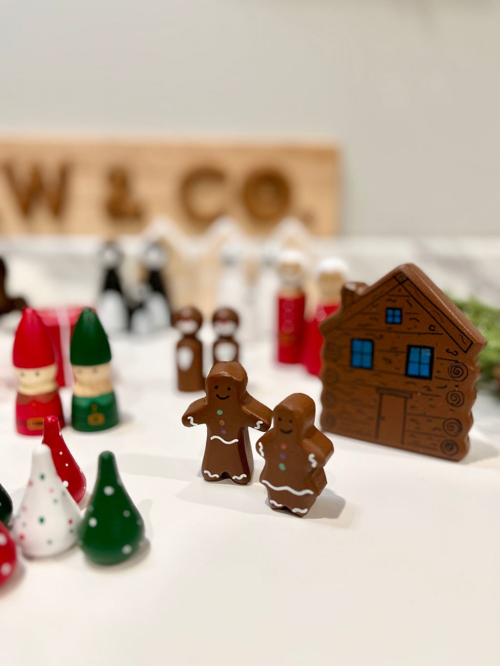 Gingerbread man and woman figurines with wooden house, elf dolls, and colorful cone-shaped decorations on white surface
