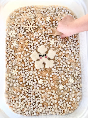 Winter sensory bin filled with white beans, rice, wooden snowflakes, and a felt snowflake with a wooden spoon handSubview