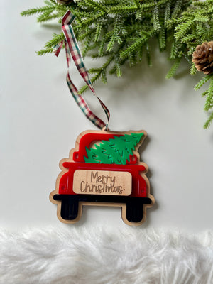 Wooden red truck ornament carrying green Christmas tree with engraved Merry Christmas sign and plaid ribbon